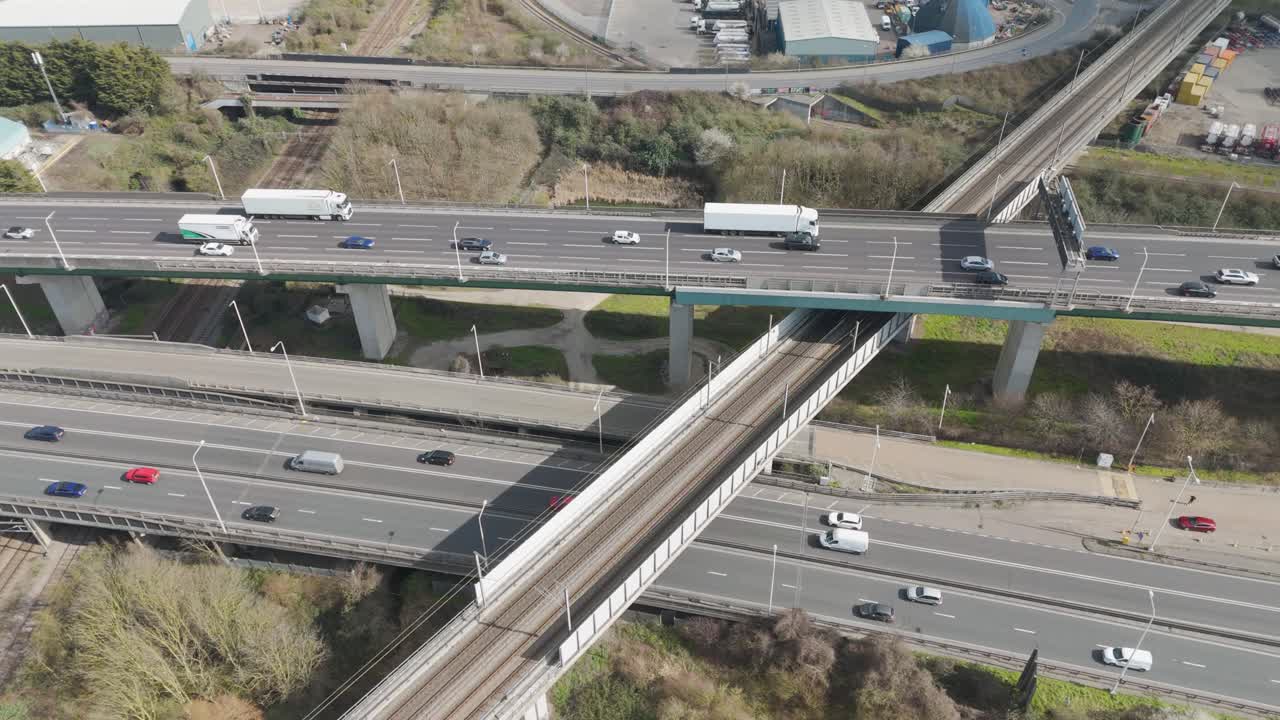 Dynamic aerial over multilane A282 interchange as streams of cars and lorries traverse stacked bridges and ramps through Thames-side transport hub