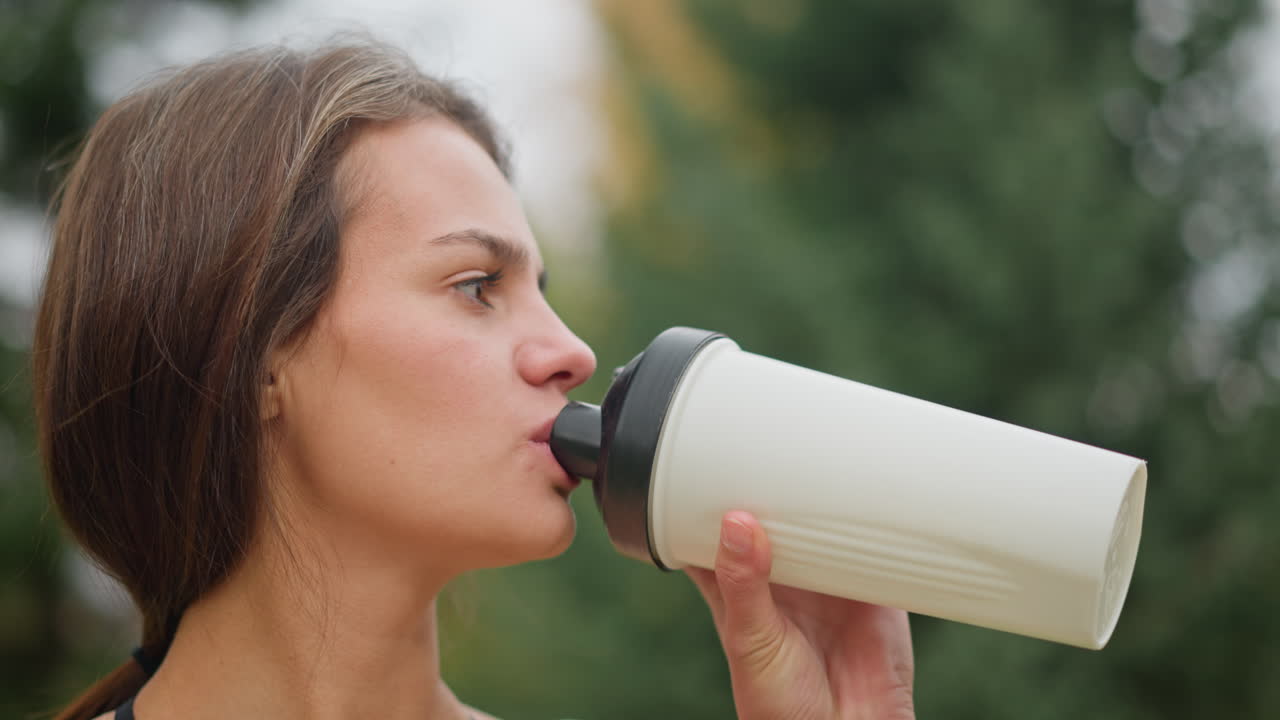 Portrait view of a lady drinking water from her bottle, focusing on hydration during outdoor activity, her focus on refreshing herself highlights wellness and fitness routines