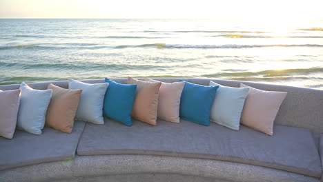 A-colorful-row-of-decorative-pillows-along-the-back-of-a-seat-looking-out-at-the-ocean