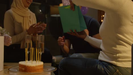 multi-cultural friends giving man birthday present at home with cake and candles at party 1