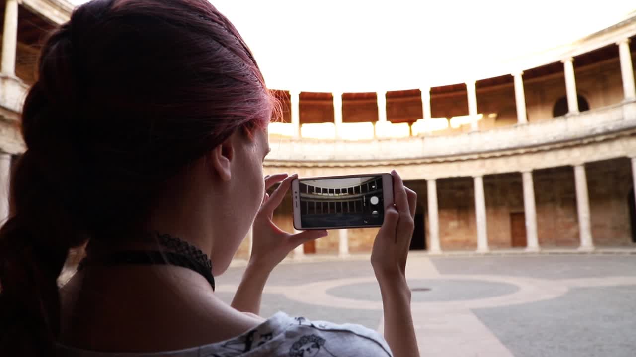 chica pelirroja haciendo una fotografía con un smartphone a un monumento en granada, españa