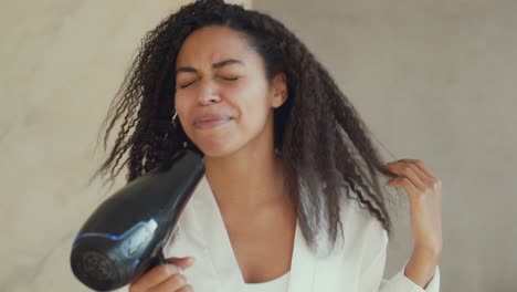 diversión matutina doméstica. joven positiva mujer afroamericana secando su cabello rizado y cantando en el secador de cabello en el baño