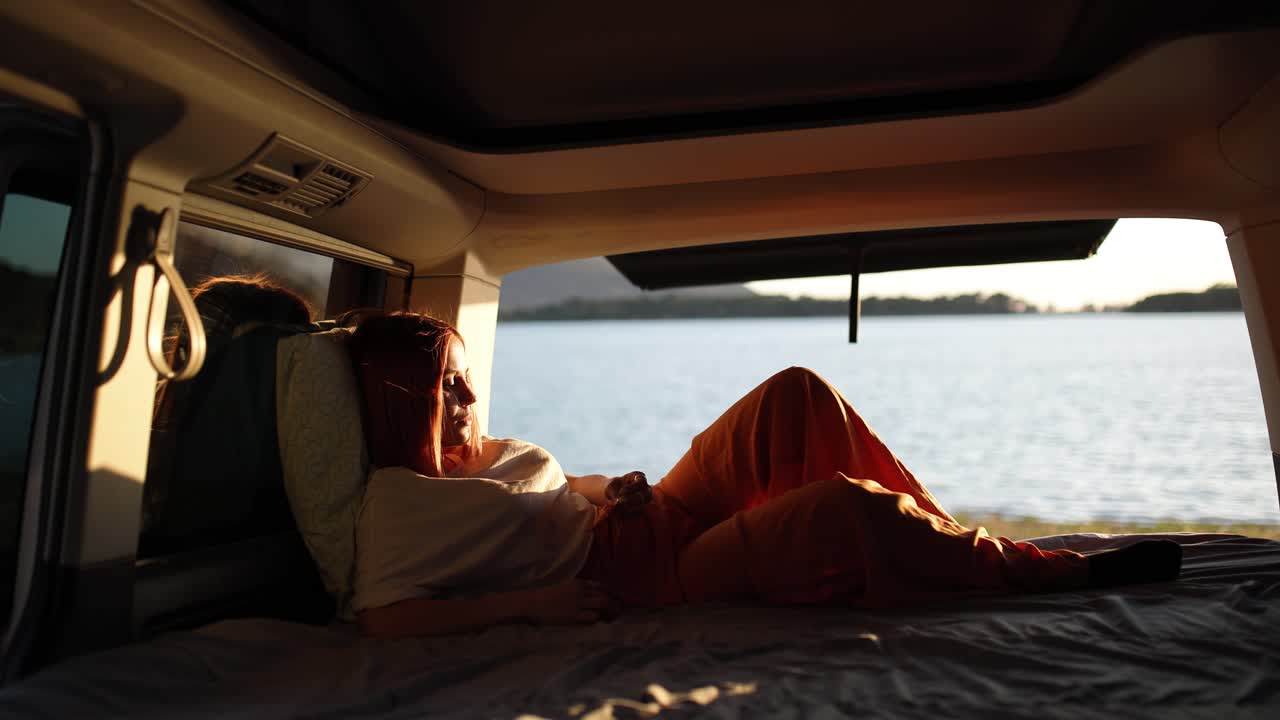 Donna che si rilassa in un camper guardando il lago al tramonto.