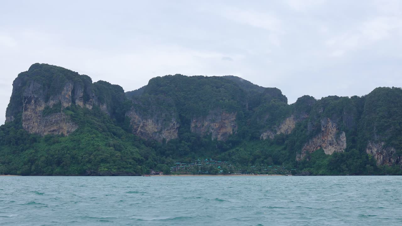 무지한 하늘 아래의 크라비의 놀라운 석회암 절벽과 울창한 초록색을 보여주는 조용한 보트 여행, 부드러운 움직임으로 포착