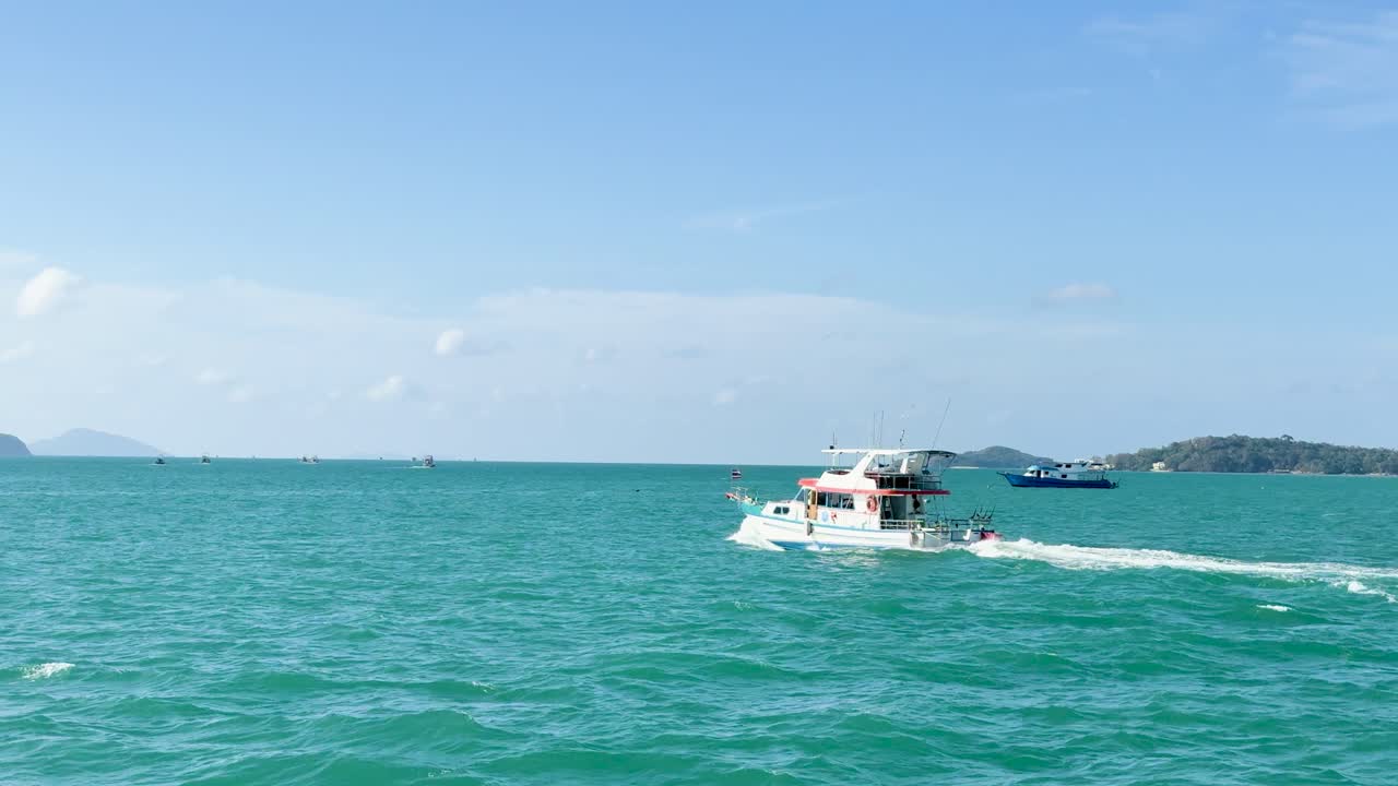 A boat travels across turquoise waters under clear skies in Chalong Bay, Phuket, capturing serene oceanic beauty