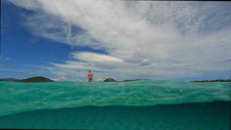 half underwater pov of man having fun practicing sup on surf board or standup paddleboard over sea water surface