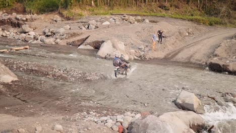 Ein-Paar-Fährt-Mit-Dem-Dirtbike-Durch-Den-Fluss-Und-Hebt-Die-Beine-An,-Um-Nicht-Nass-Zu-Werden