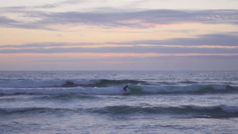 A-Surfer-Catching-a-Wave-in-Guincho-Beach,-Portugal-during-a-Blue-Hour