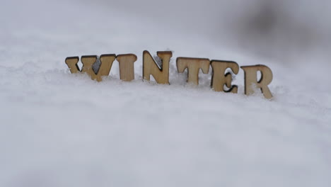 the word winter written with wooden letters on snow, rack focus tilt up