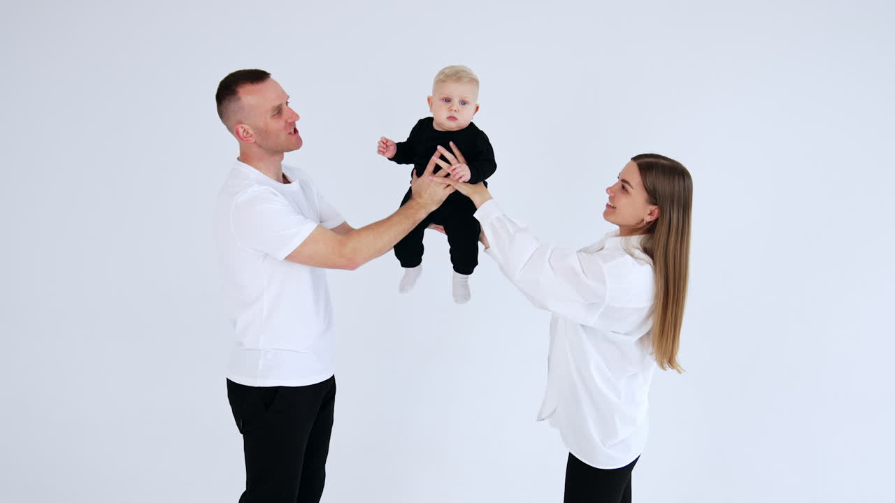 Happy smiling mom and dad hold a little baby boy. Loving proud parents kiss their son on the cheeks. White backdrop.