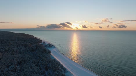 aerial establishing footage of trees covered with snow, sunny winter day at the sunset, golden hour, nordic woodland pine tree forest, baltic sea coast, wide drone shot moving forward