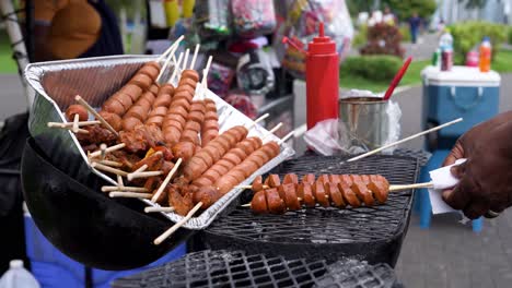 selling street food in panama: picking skewered food being grilled , with bottles of barbecue sauce