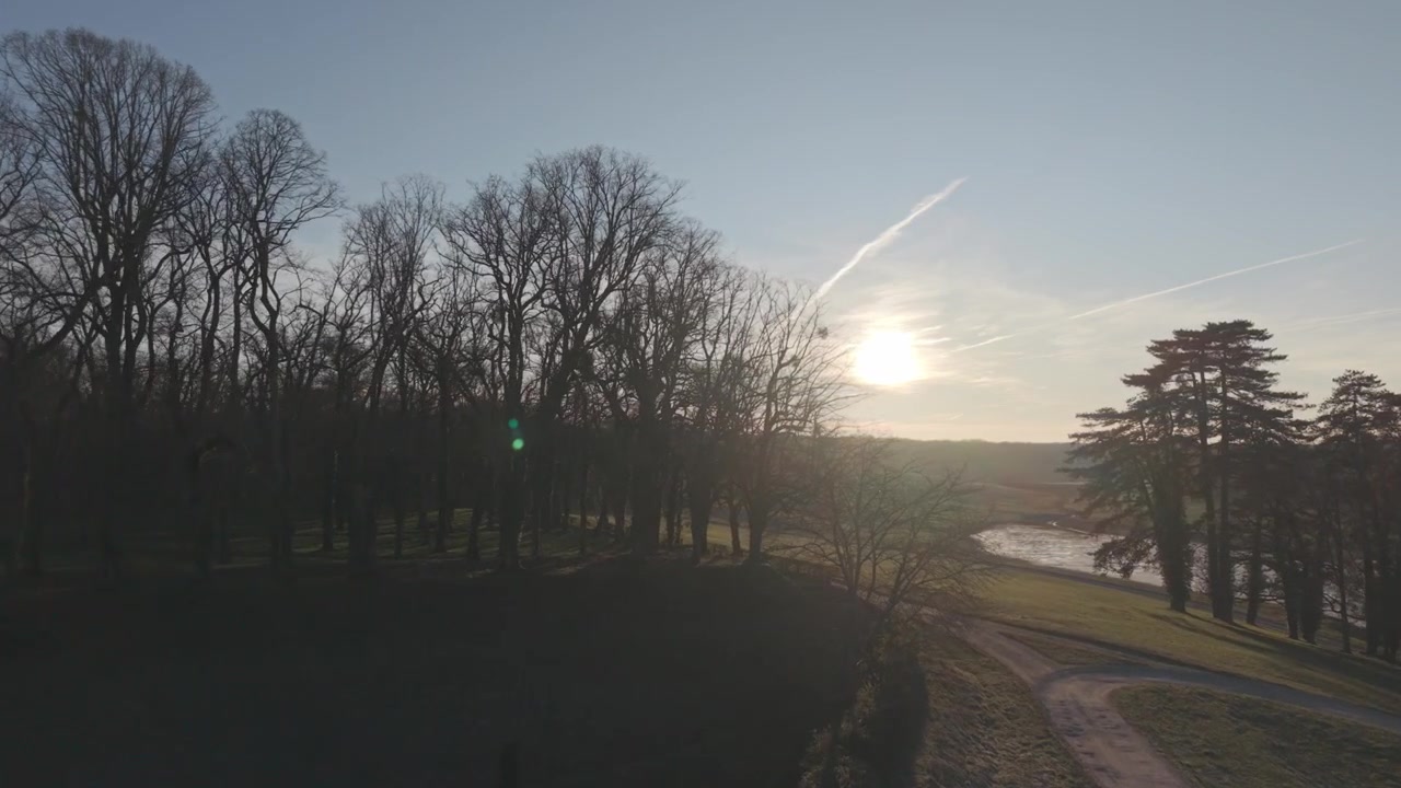 An aerial view drifts through silhouetted trees in a park as the sun sets in the Loire Valley, France.