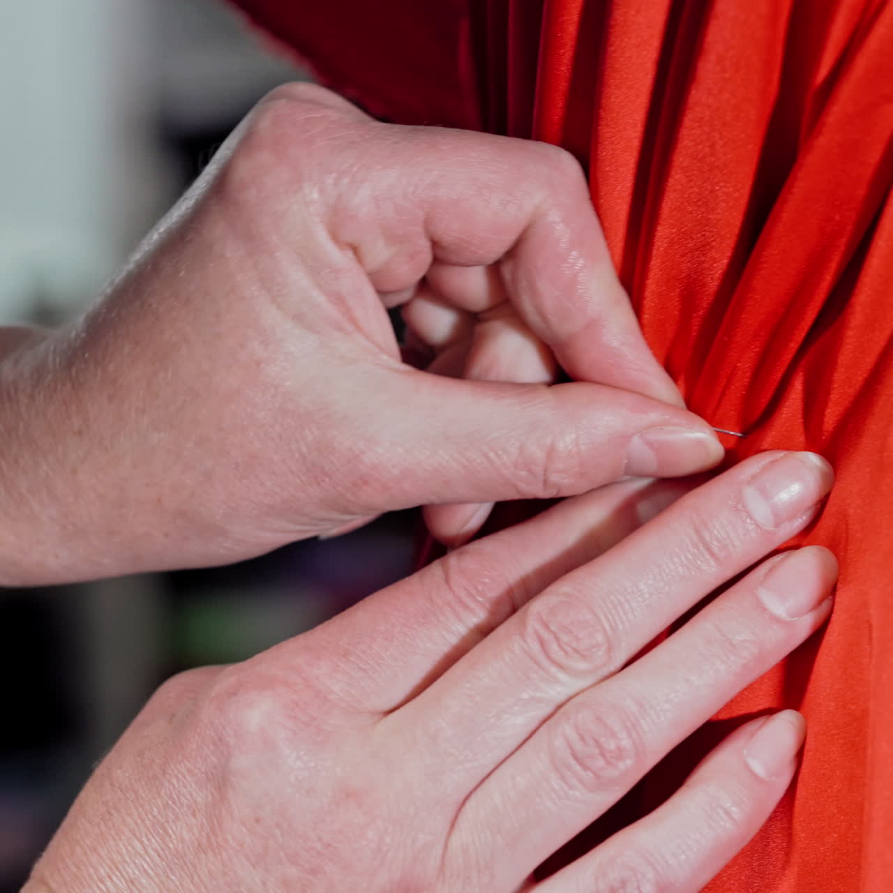 Hands of a professional tailor working with red cloth on mannequin with pins. Seamstress pinning on red fabric on the dummy to sew a nice dress. Close-up.