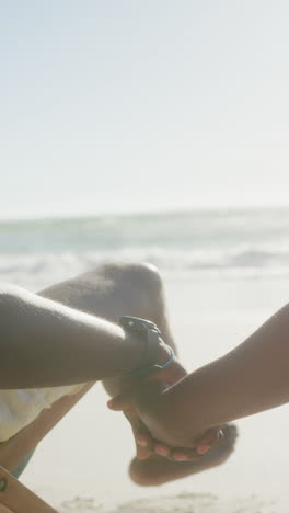 vertical video of senior african american couple holding hands at beach, in slow motion