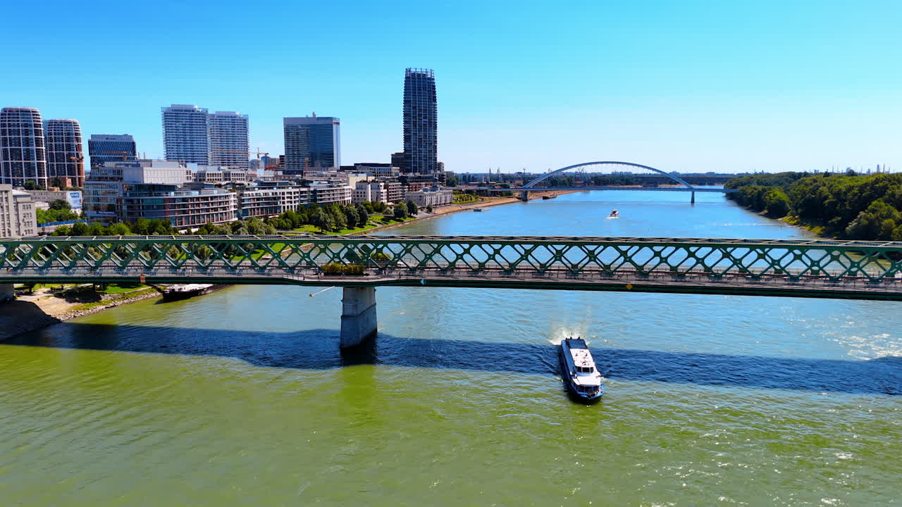 The Old Bridge connecting the banks of the Danube. A riverboat passes under the bridge. Skyline of Bratislava and the Appolo Bridge at backdrop