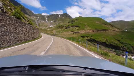 a grey car’s point of view on the majestic transfagarasan mountain road, with towering mountain peaks and a clear blue sky in the background