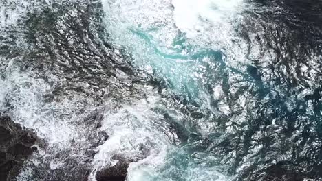 birds eye view of blue ocean waves smashing onto rocks