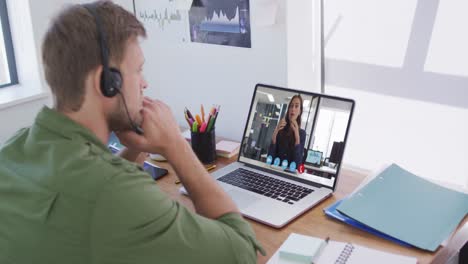 Caucasian-man-wearing-phone-headset-having-a-video-call-with-female-colleague-on-laptop-at-office