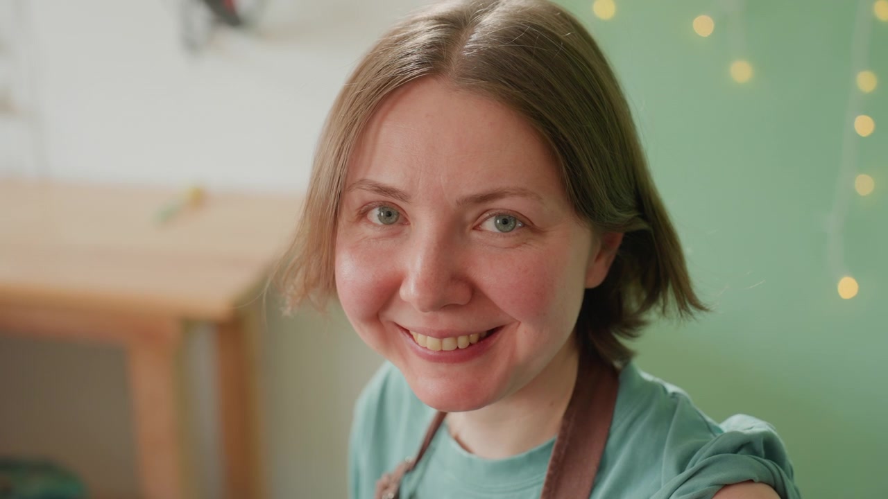 Kunstner slapper af blandt atelierudstyr. Smilende pottemager i hyggeligt værksted med værktøj og varm belysning. Nyder et fredfyldt øjeblik i et indbydende atelier fyldt med håndlavede genstande og blød belysning.