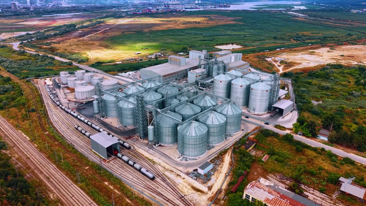 Instalação de armazenamento de grãos com silos e trilhos de trem perto de um rio. Uma grande instalação de armazenamento de grãos fica ao lado de um rio com silos e trilhos de trem à vista.