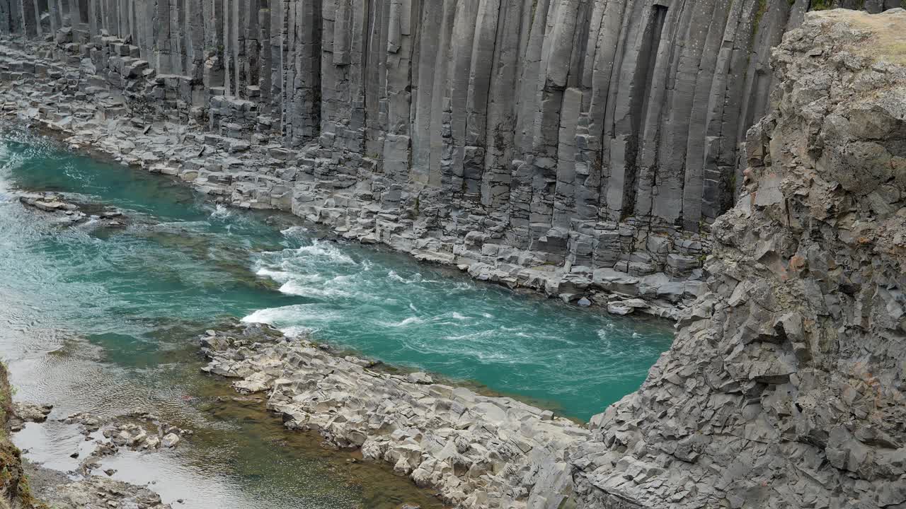 웅장한 바살트 조형물들이 아이슬란드의 아름다움 속의 평온한 파란 강을 고 있습니다.