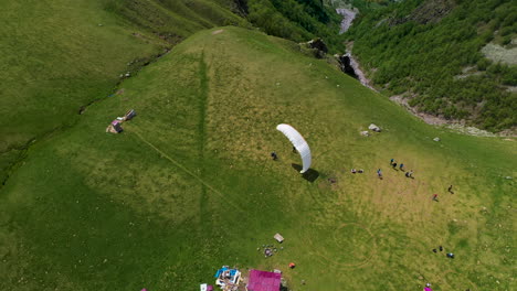 downward angle drone shot of a paraglider landing on a mountaintop in gudauri georgia