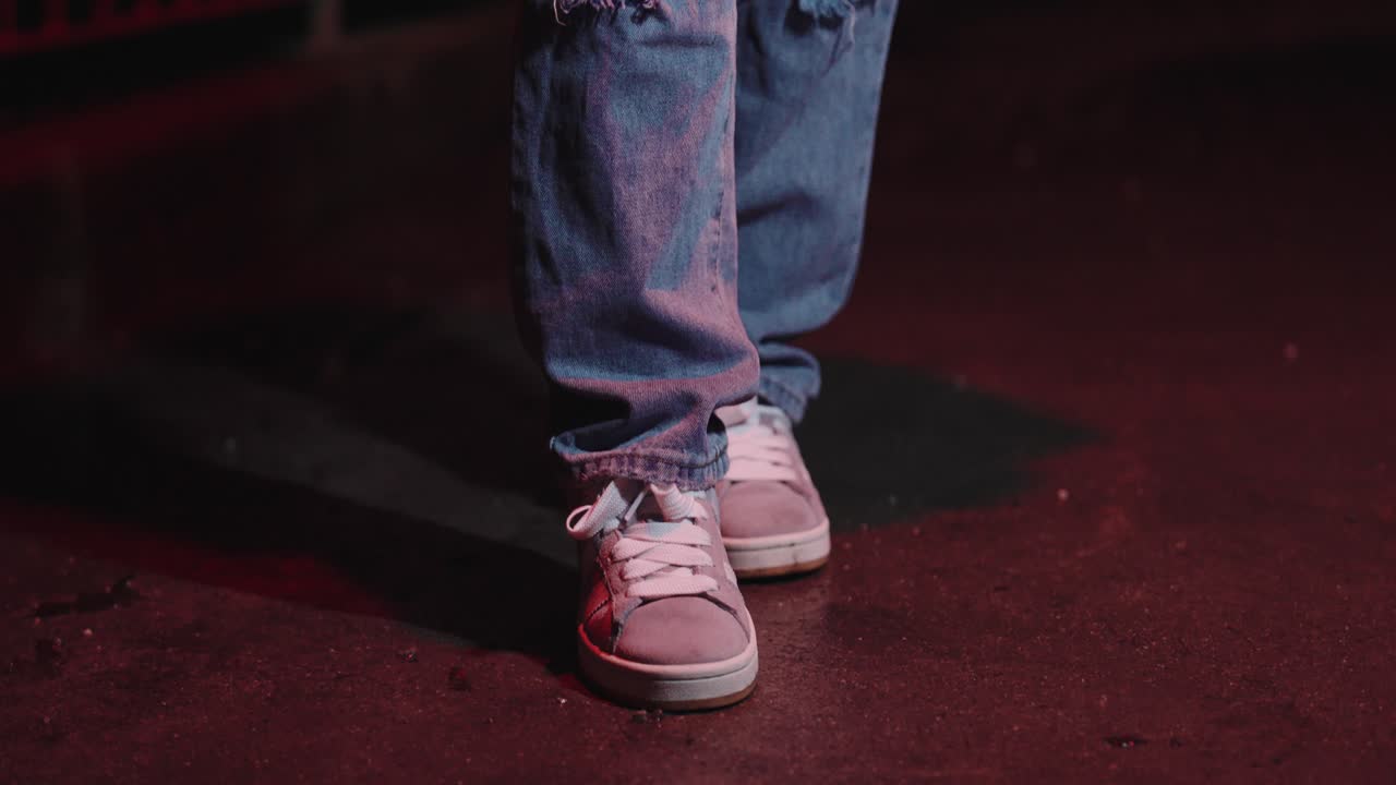 Young beautiful woman in sneakers and ripped jeans on the street at night