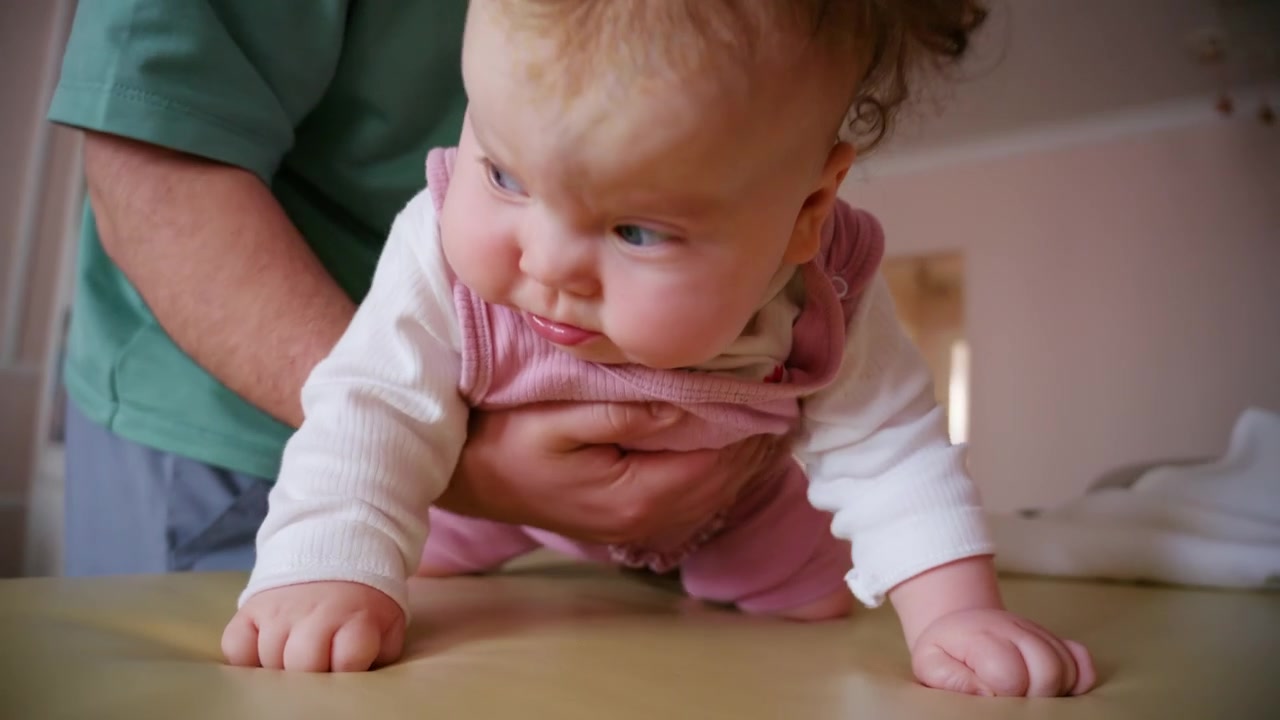 Close up footage of a caregiver gently caring for an infant lying on a cushioned changing mat indoors