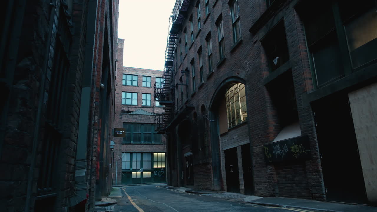 Early morning view of a Manchester backstreet with metal fire escape staircases on buildings, captured in a panning down shot with low light
