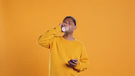 Man-enjoying-fresh-coffee-from-disposable-paper-cup,-studio-background