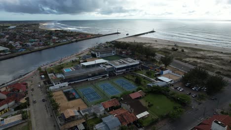 side drone tracking shot of beautiful tennis courts located near the beach and the sea in the background