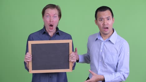 businessman showing shocking news while man is holding blackboard against green studio background