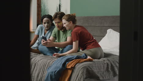 three rommates with facial mask watching smartphone sitting on the bed in bedroom 1