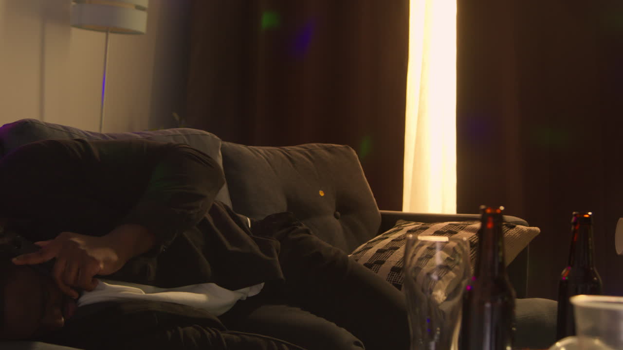 집 파티에서 알코올을 마신 후 소파에서 깨어난 남자가 숙취로 고통 받고 휴대 전화로 이야기하고 있습니다.