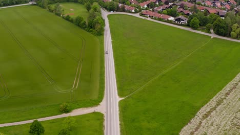 camera downswing of a drone which follows a car coming out of a town driving down a road at springtime from a high angle view