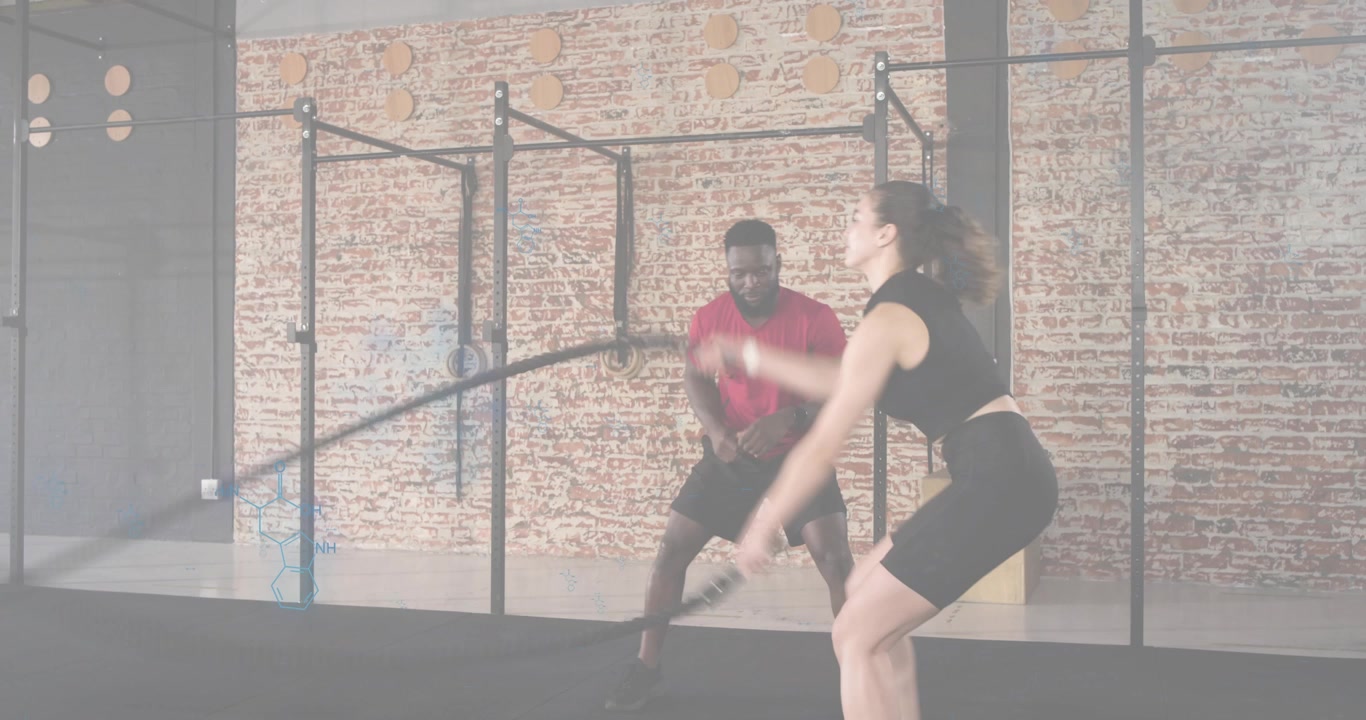Personal trainer che fa segno al cliente di iniziare le sbattute con le battle rope, guidando il posizionamento contro una struttura in mattoni