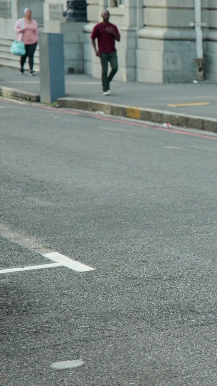 Vertical video: Entering right pedestrians walking by stone facade, man in blue tank holding duffel