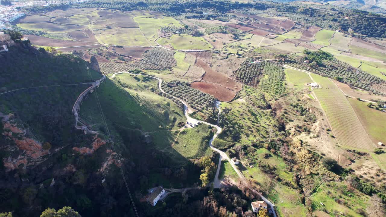 Aerial pan across homes on Ronda cliffs over agriculture farms then back