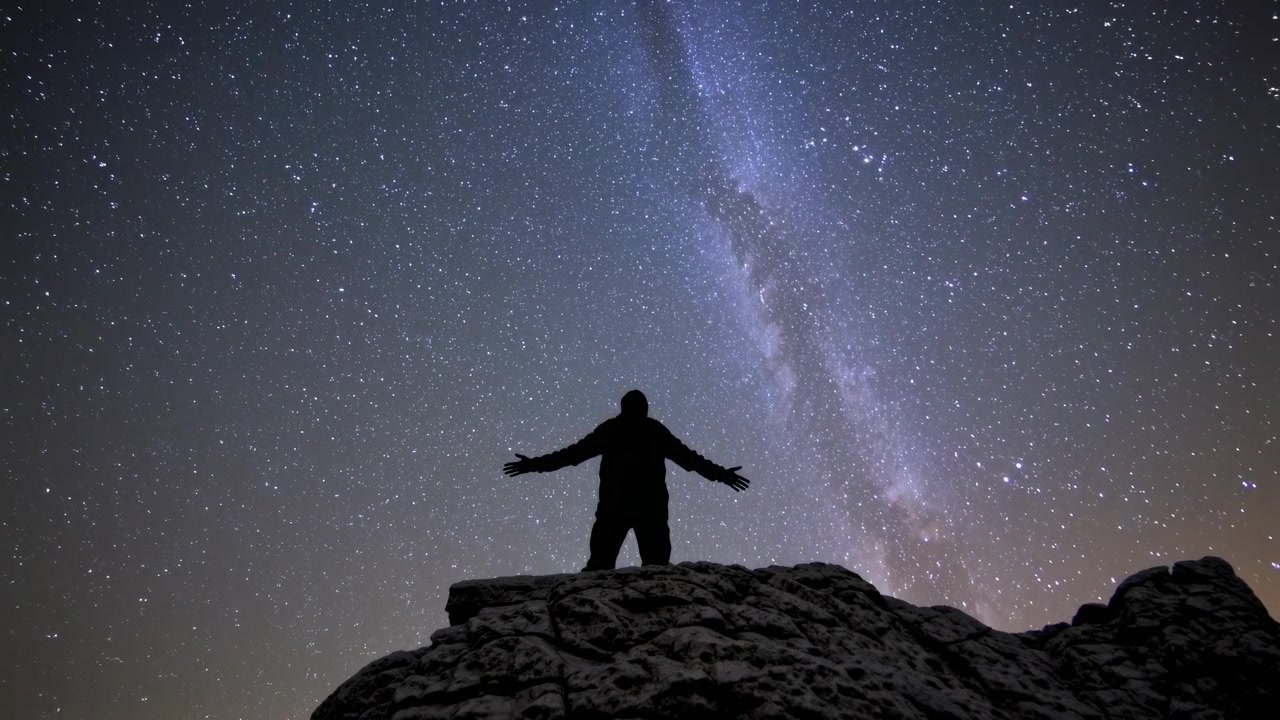Lapso de tiempo de una persona en la cima de una montaña bajo la Vía Láctea estrellada