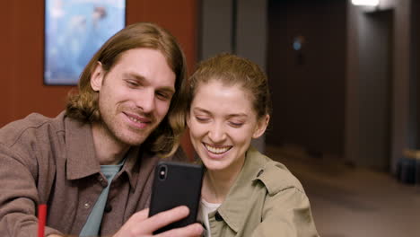 happy caucasian couple having fun while taking a selfie with phone at the cinema