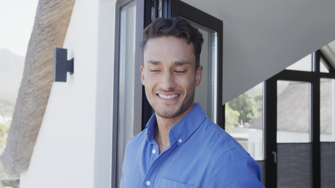 feliz hombre biracial de pie en el balcón soleado sonriendo, cámara lenta
