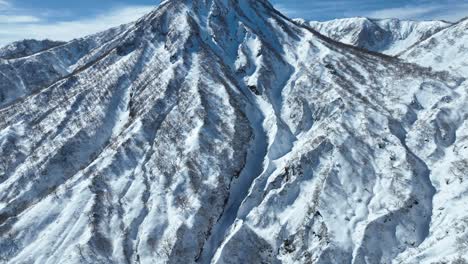 Aerial-wide-establishing-shot-pan-up-revealing-mountain-Japan-mount-myōkō,-on-a-clear-winter-day,-a-volcanic-mountain-in-Myoko-Togakushi-Renzan-National-Park-region