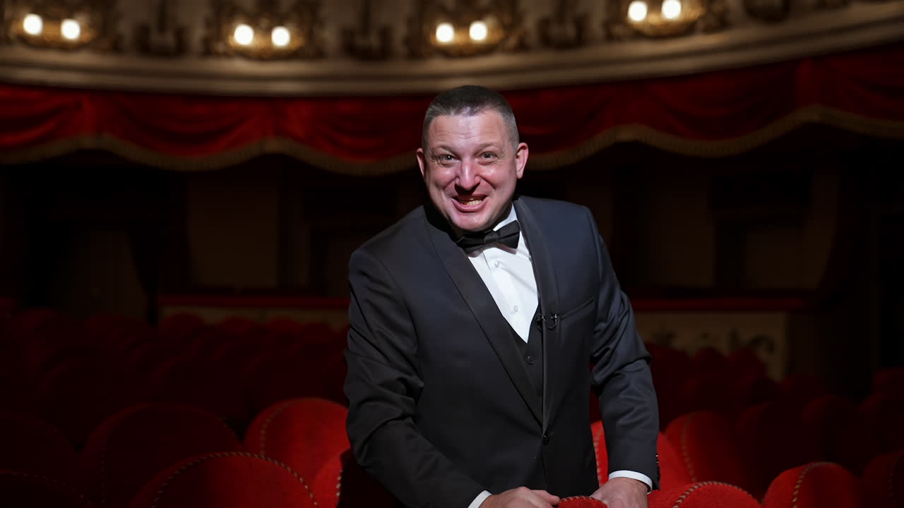 Man in empty theater hall points on a hand with watch and waits for performance beginning. Ready to watch visitor.