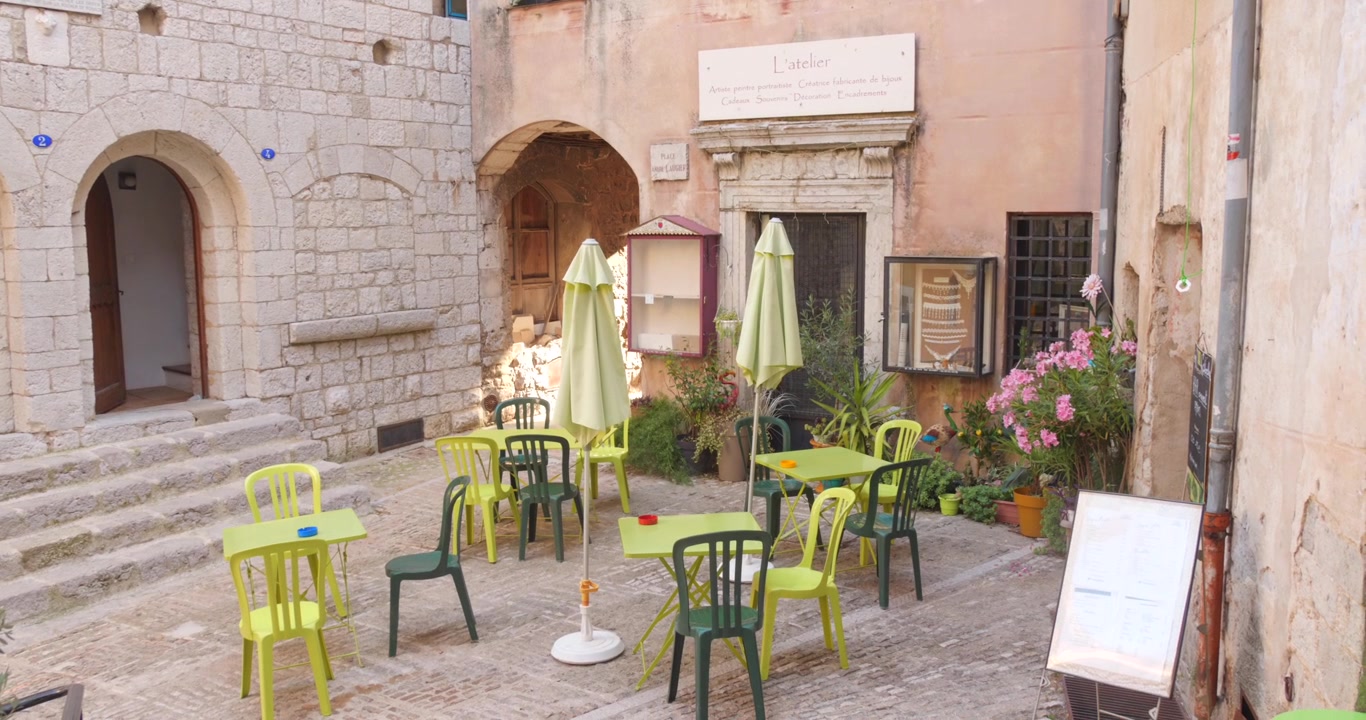 Tavoli e sedie di un caffè all'aperto in un tranquillo cortile medievale in pietra, borgo di Peille