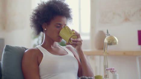 medium shot of a black woman drinking tea while using mobile phone