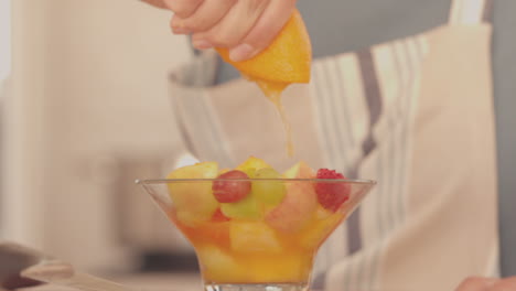 woman squeezing orange over her fruit salad