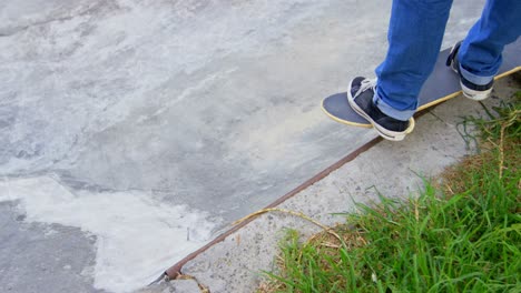 Low-section-of-young-man-standing-on-skateboard-in-skateboard-ramp-at-skateboard-park-4k