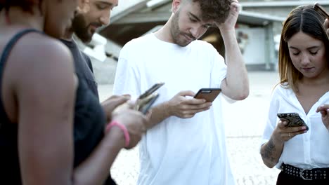 serious friends standing in circle on square with phones