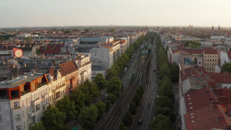 Forwards-fly-above-wide-boulevard-Schoenhauser-Allee-with-elevated-railway-track-and-train-station.-Morning-aerial-view-of-urban-neighbourhood.-Berlin,-Germany